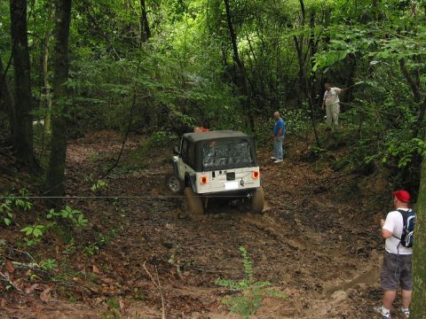 2000 Jeep Grand Cherokee - A white Jeep Wrangler struggles through a muddy off-road path, with onlookers observing the challenging terrain.