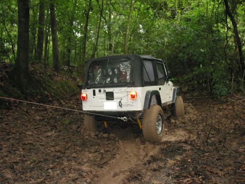 2000 Jeep Grand Cherokee - White Jeep Wrangler with soft top stuck in thick mud on a wooded trail, being pulled by a rope.