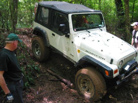 2000 Jeep Grand Cherokee - A white Jeep Wrangler Rubicon navigates a challenging muddy off-road course with onlookers present.