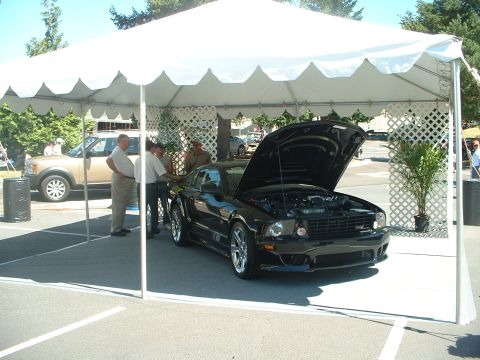 1999 Ford Crown Victoria - A black Ford Mustang is displayed under a tent at a car show, with its hood open, revealing the engine.