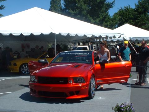 1999 Ford Crown Victoria - Red Saleen convertible on display with a yellow Mustang behind it at an outdoor car show.