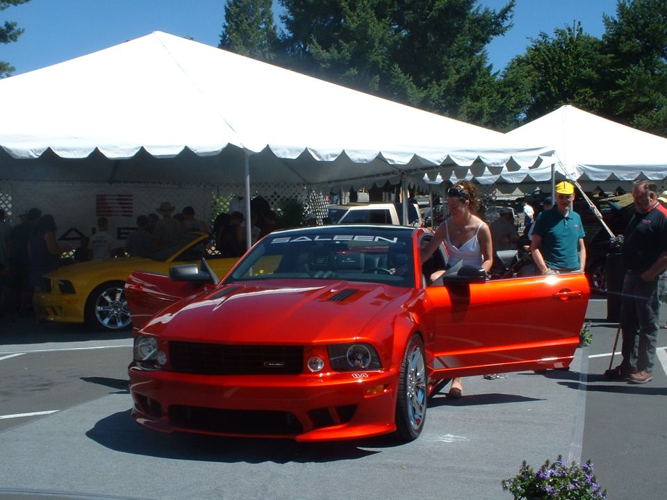 Red Saleen convertible with door open, yellow Mustang in background under tent