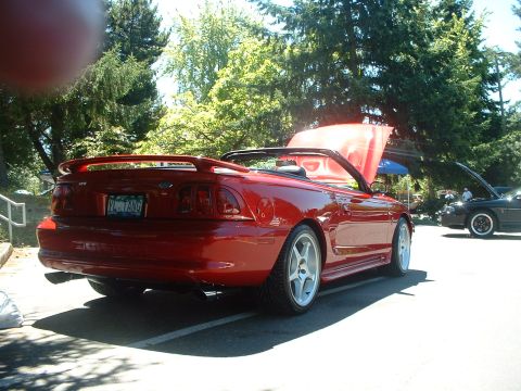 1999 Ford Crown Victoria - A red convertible is parked outdoors with its hood up, alongside another car.