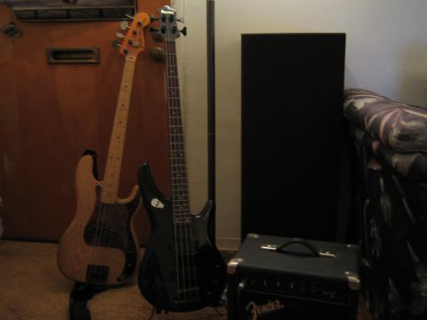 1990 Ford Bronco - Two electric bass guitars stand against a wood door next to a tall speaker and a black Fender amplifier in low light.