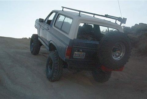 1986 Ford Bronco - A modified Ford Bronco with off-road tires navigates a sandy incline under a clear sky.