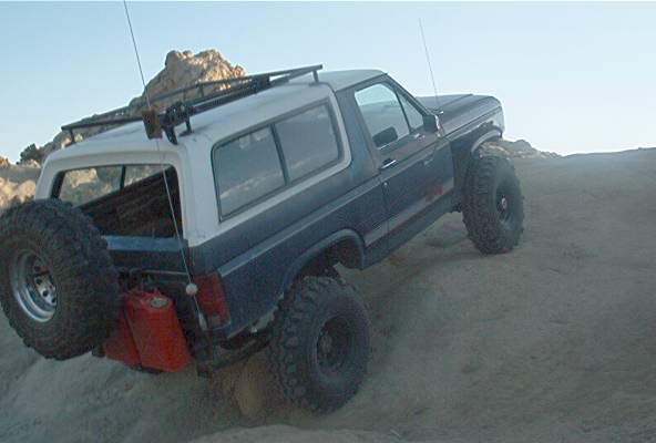Blue and white Ford Bronco with spare tire and gas cans on rocky terrain