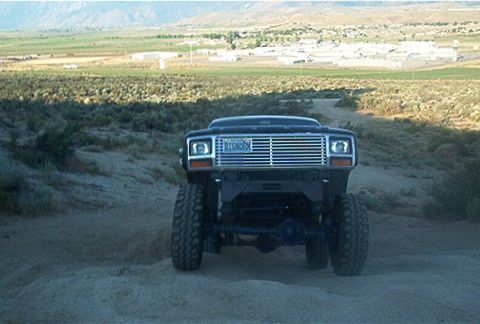 1986 Ford Bronco - A lifted black Ford Bronco is seen from the front on a dusty trail with mountains in the background.