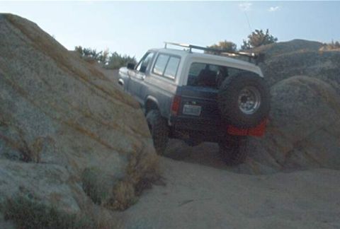 1986 Ford Bronco - Ford Bronco navigating a challenging off-road trail with large rocks and sand.