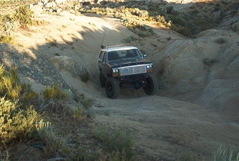 1986 Ford Bronco - Ford Bronco navigates a challenging off-road trail in a desert landscape.