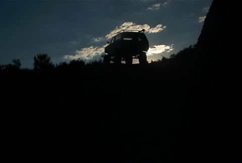 1986 Ford Bronco - An SUV is parked on a grassy hill with clouds in the sky.