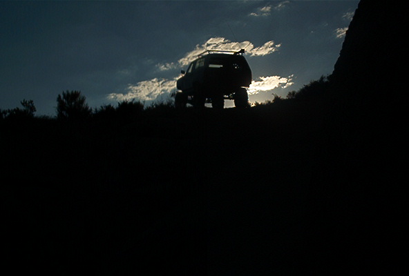 SUV silhouetted against cloudy sky on a hill