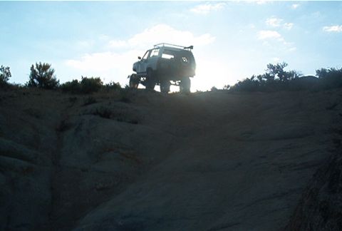1986 Ford Bronco - A lifted SUV navigates a challenging off-road terrain under a bright sky.
