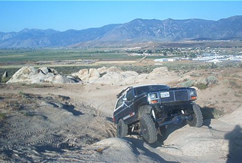 1986 Ford Bronco - This lifted Ford Bronco navigates a rocky, off-road terrain with a mountainous landscape in the distance.