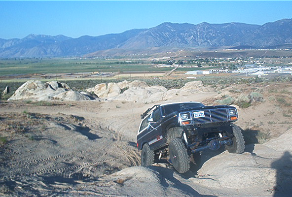 Black Ford Bronco climbing over rocks on a dirt trail, mountains in background