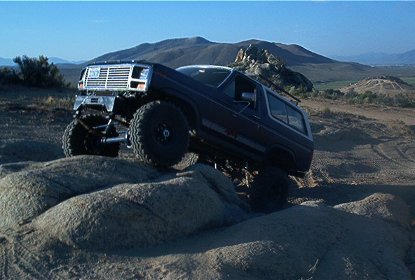 Dark blue 1980 Ford Bronco with lifted suspension and large tires climbing rocks