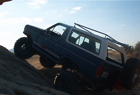 Blue SUV with white top climbing a rocky incline, sky in background