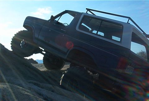 1986 Ford Bronco - This modified SUV navigates a challenging rocky terrain under a clear blue sky.