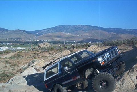 1986 Ford Bronco - Ford Bronco navigates a steep, rocky incline under a clear blue sky.