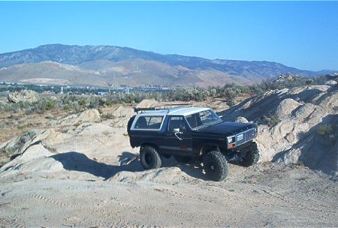 1986 Ford Bronco - 1986 Ford Bronco navigating rough, rocky terrain under a clear blue sky.