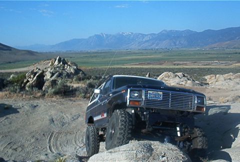1986 Ford Bronco - This lifted 1986 Ford Bronco navigates a , rocky landscape under a clear blue sky.
