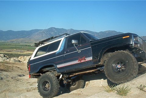 1986 Ford Bronco - Modified Ford Bronco navigating rough terrain under a clear blue sky.
