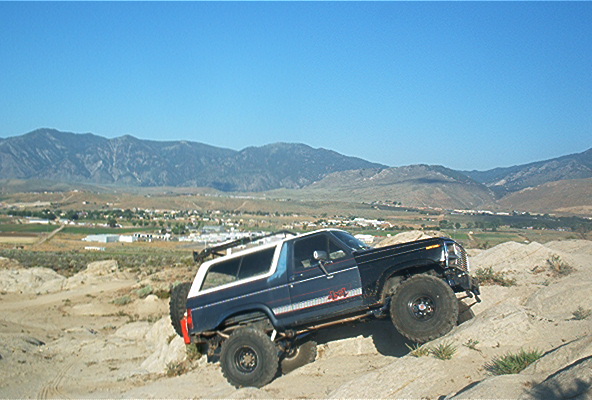 1986 Ford Bronco climbing a dirt hill with mountains in the background