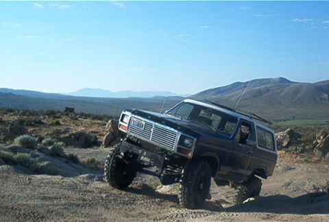 1986 Ford Bronco - Ford Bronco navigating a rocky, off-road trail under a clear blue sky.