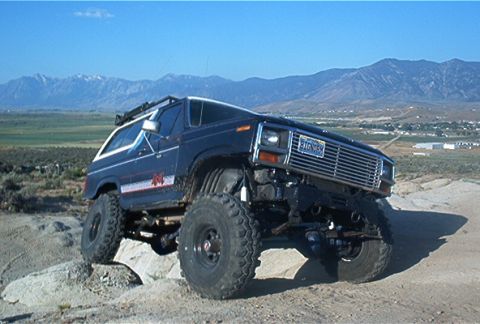 1986 Ford Bronco - This modified SUV is navigating a rocky, off-road trail with mountains visible in the distance.