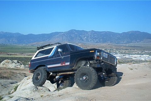 1986 Ford Bronco - A modified Ford Bronco navigates a rocky, off-road landscape under a clear blue sky.
