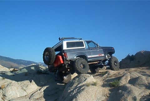 1986 Ford Bronco - Modified 1986 Ford Bronco navigating a rocky off-road trail under a clear blue sky.
