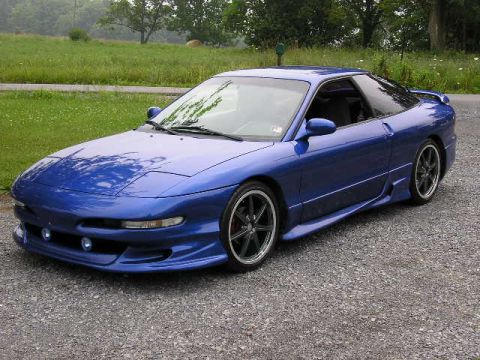 1994 Ford Probe - A blue 1994 Ford Probe is shown from a three-quarter front angle, parked on a gravel surface with a grassy field in the background.