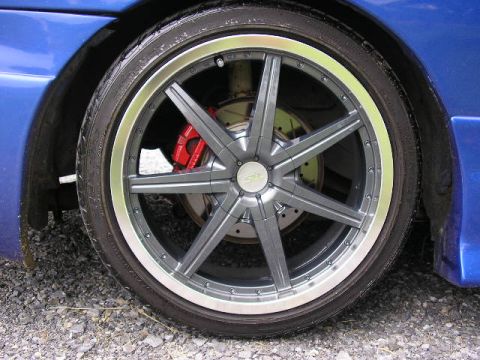 1994 Ford Probe - A close-up view of a custom gray wheel and red brake caliper on a blue vehicle.