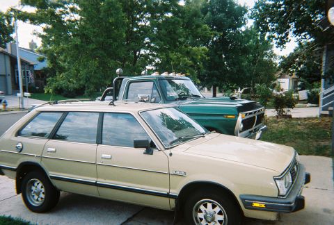 1972 Ford Ranchero - A tan Subaru station wagon is parked in front of a green Ford pickup truck on a residential street.