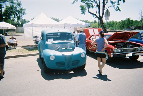 1972 Ford Ranchero - A blue coupe with its hood open is parked at an outdoor car show next to a red muscle car.
