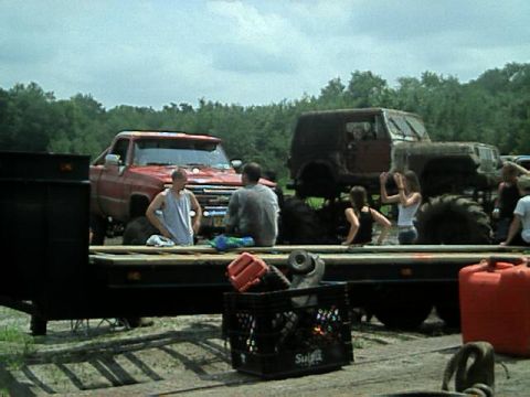 1987 Suzuki Samurai - Several people gather around a red pickup truck and a lifted Jeep, with a trailer in the foreground.