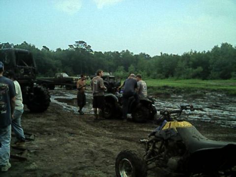 1987 Suzuki Samurai - Several people stand around ATVs and a large truck in a muddy, outdoor scene.