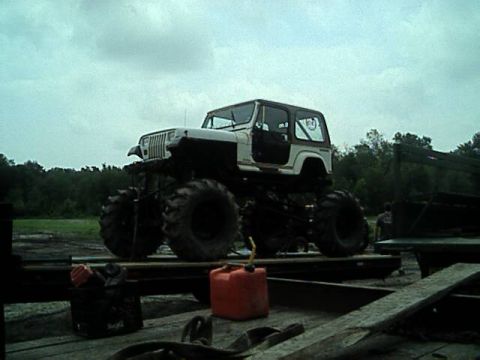 1987 Suzuki Samurai - This lifted monster truck, likely a Jeep, sits on a trailer with two gas cans nearby.