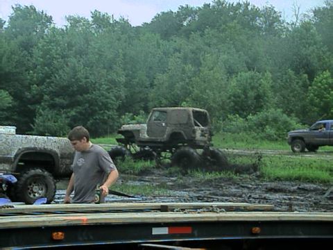 1987 Suzuki Samurai - Off-road vehicles navigate a muddy terrain surrounded by dense trees.