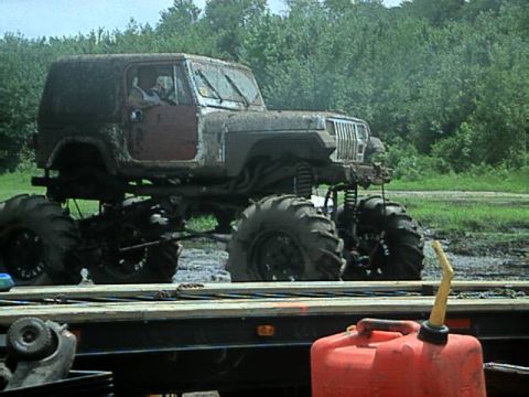 1987 Suzuki Samurai - A heavily modified Jeep Wrangler with oversized tires is shown in a muddy outdoor setting.