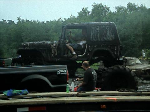 1987 Suzuki Samurai - A heavily mud-caked Jeep Wrangler sits off-road with a pickup truck nearby.