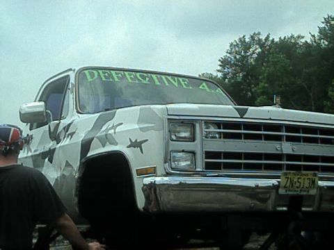 1987 Suzuki Samurai - Pickup truck with a custom camouflage wrap and 'DEFECTIVE 4x4' decal on the windshield.