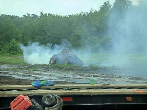 1987 Suzuki Samurai - A vehicle is seen emitting smoke in a muddy field, with trees lining the horizon.