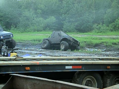 1987 Suzuki Samurai - An off-road vehicle is stuck in the mud next to a trailer, with another vehicle visible in the background.