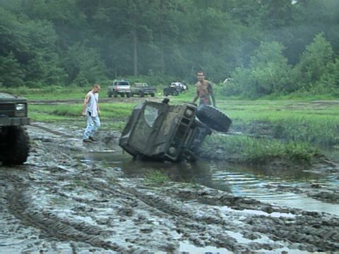 1987 Suzuki Samurai - Multiple off-road vehicles are present at a muddy track, with one vehicle overturned in the water.