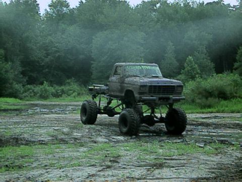 1987 Suzuki Samurai - A heavily modified pickup truck sits in a muddy outdoor area with trees in the background.
