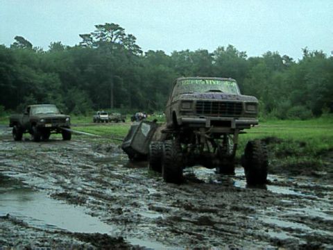 1987 Suzuki Samurai - Two trucks are engaged in mud bogging, with one truck appearing to be stuck in the mud while the other attempts to pull it.