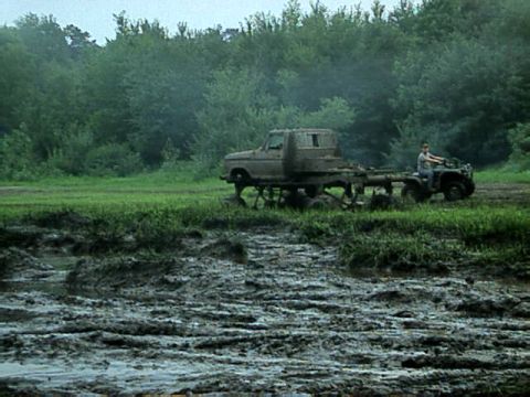 1987 Suzuki Samurai - A truck and an ATV navigate a very muddy terrain with trees in the background.