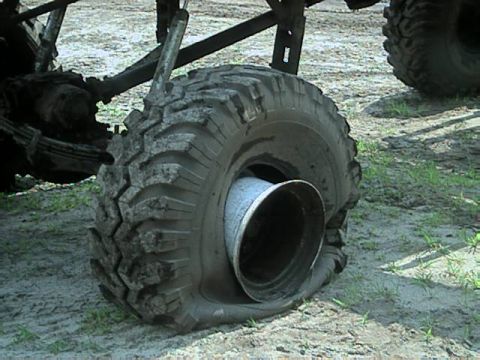 1987 Suzuki Samurai - A vehicle's tire is completely flat, revealing the rim and part of the suspension system.