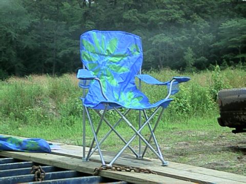 1987 Suzuki Samurai - A blue folding chair sits on a wooden platform outdoors, with a vehicle partially visible to the right.