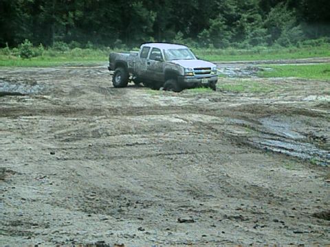1987 Suzuki Samurai - A pickup truck is stuck in a muddy field with trees in the background.